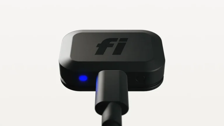 Fi Mini tracker with a black USB-C cable plugged into its end and a blue charging light glowing