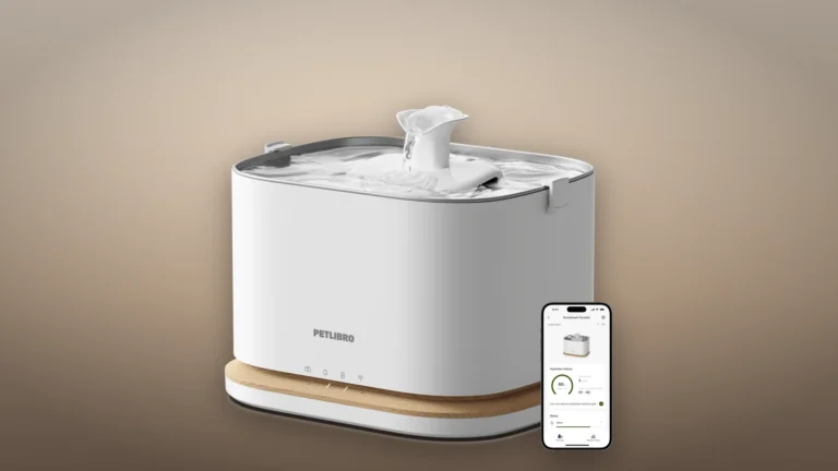 White PETLIBRO Dockstream 2 Smart Cordless Fountain with a walnut-tone base and a phone showing the PETLIBRO app, on a warm bedside backdrop